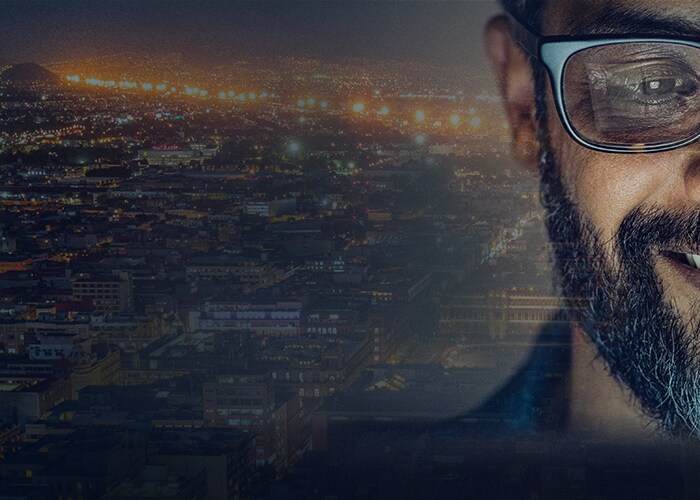 Carreiras em tecnologia na Maersk - Funcionário sorri, com cidade iluminada à noite em segundo plano.