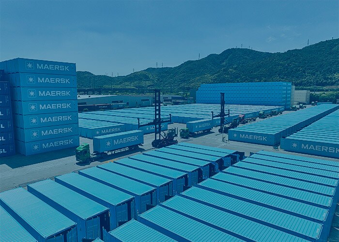 A large Maersk logistics facility with rows of shipping containers, trucks, and container-handling equipment