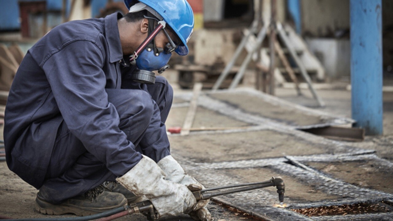 Man, hardhat, goggles, gloves, cutting metal sheet
