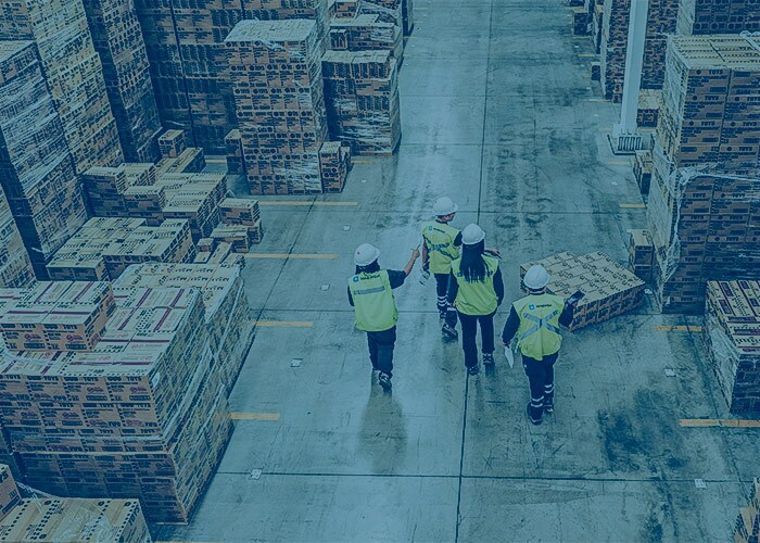 Warehouse team walking through a large storage facility with stacked pallets and boxes
