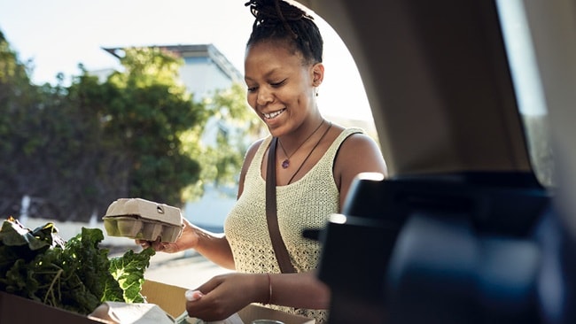 Woman smiling and putting newly bought groceries in the trunk of her car