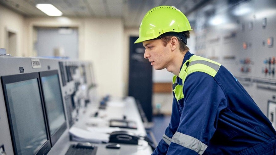 A supply chain worker, dressed in safety gear, looking into a computer screen in a control room