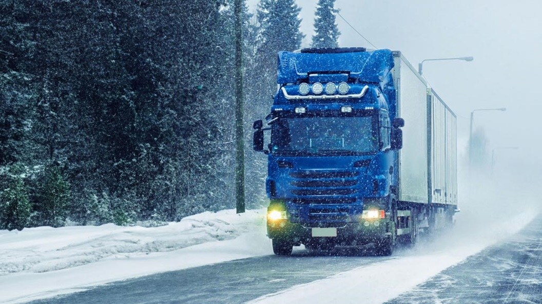 Maersk container truck driving on a winding mountain road surrounded by rocky cliffs and forest.