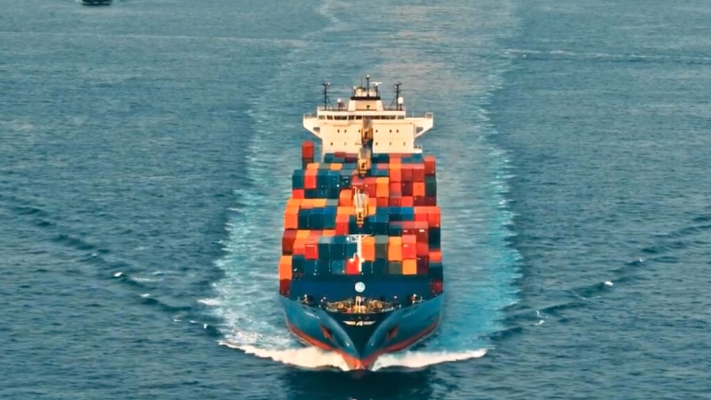 A large container ship navigates through the ocean, surrounded by blue water and a clear sky.