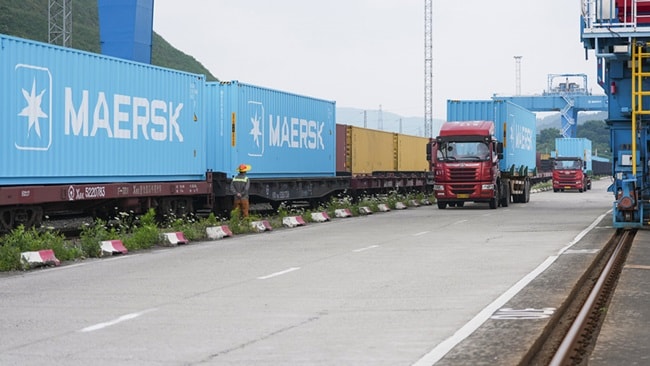 Maersk containers on rail flatcars alongside trucks at an inland intermodal freight terminal, illustrating multimodal logistics connectivity