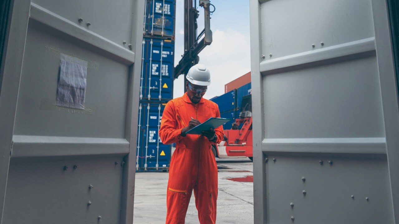 Customs clearance - A worker in protective gear standing near cargo containers