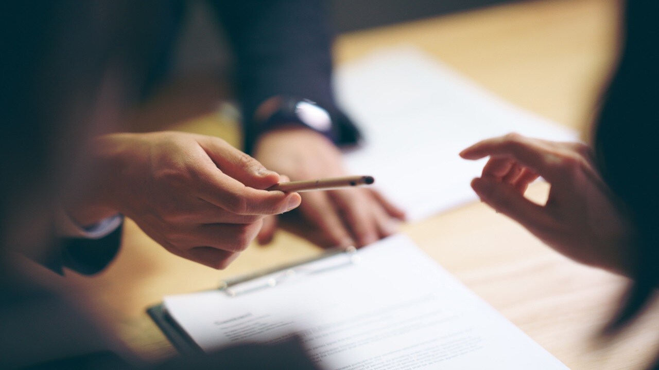 A person passing the pen to another person to sign a document