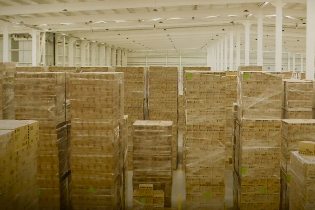 Large warehouse filled with stacks of pallets and boxes organized in rows.