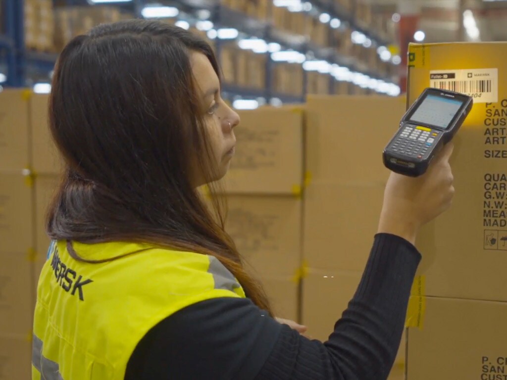 A warehouse worker scans a shipping label on a large cardboard box with a handheld device.