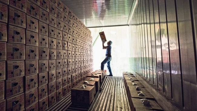 A person stands inside a storage area stacked with rows of cardboard boxes