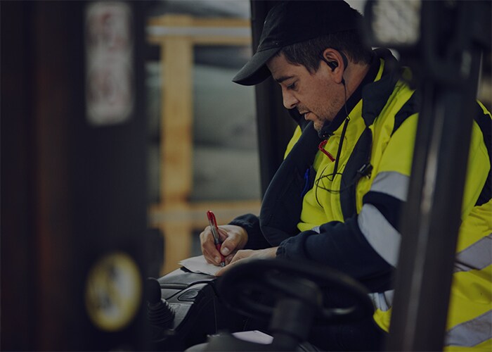 Man wearing yellow jacket on the forklift writing on notepad