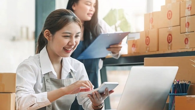 A smiling woman using a calculator and looking at a laptop