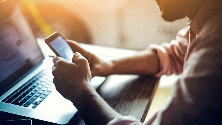 Man browsing online on laptop and mobile phone
