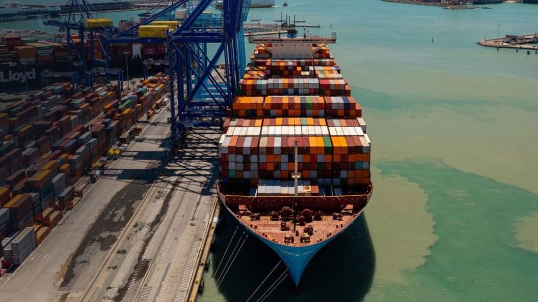 A container ship is moored at a port, surrounded by cranes and stacks of cargo containers ready for unloading.