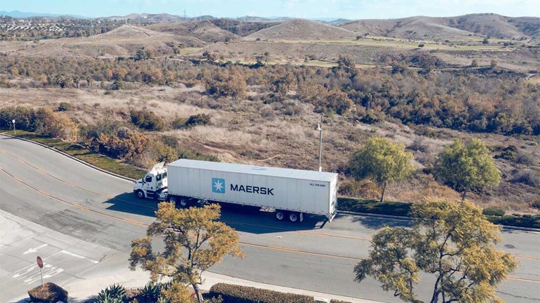 Un camión contenedor de Maersk circula por una carretera rodeada de árboles y colinas.