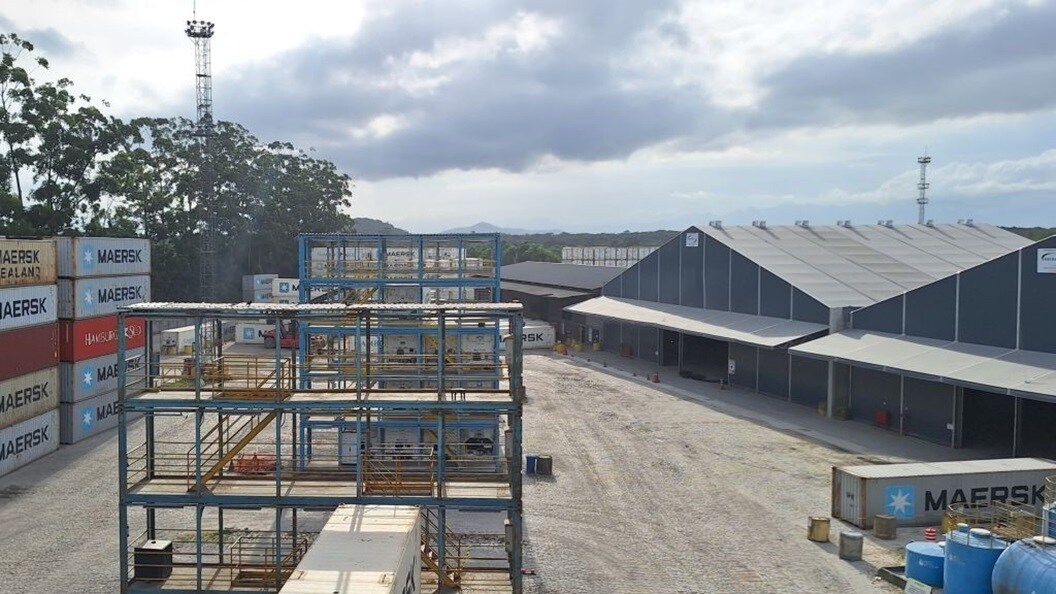 Maersk logistics facility with container stacks, warehouse buildings, and storage structures at a port location