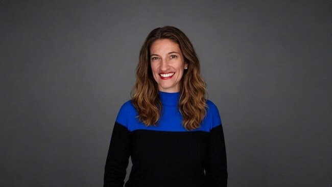 Portrait of a person in a blue and black top against a grey background.