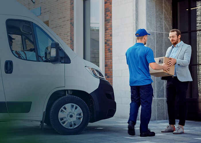 E-commerce last-mile delivery – A delivery man handing a package to a customer with a truck containing packages behind him.