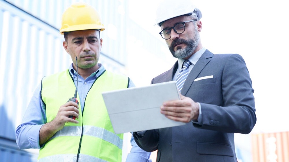 Port workers coordinating shipment details using a digital device