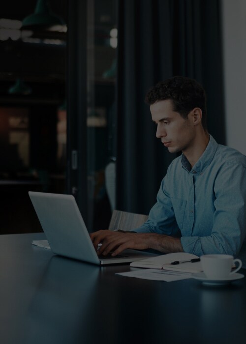 A man engaged with his laptop at a table, surrounded by a relaxed and informal setting.