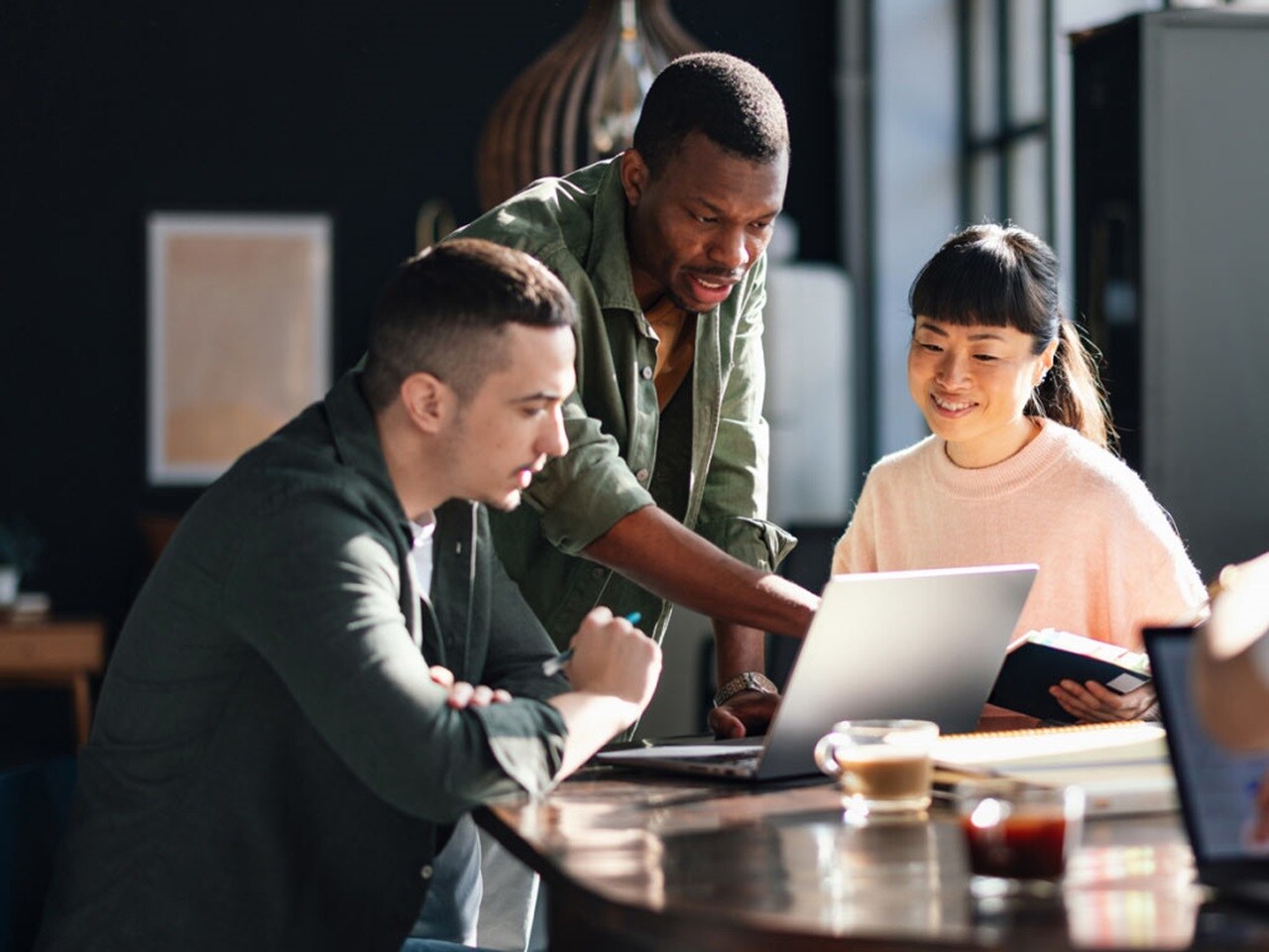 Three professionals gathered around a table and engaged in a collaborative task with a laptop.