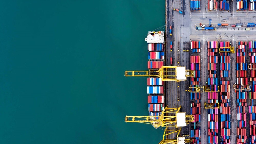 Aerial top view of a busy container port with cranes loading shipping containers and organized stacks along the terminal