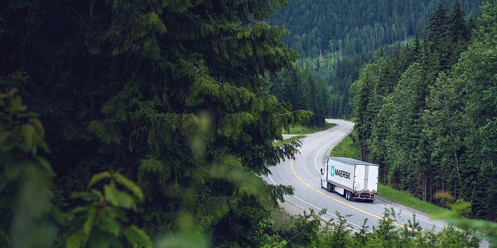 Maersk truck transporting cargo through scenic forest route, highlighting sustainable road freight logistics solutions