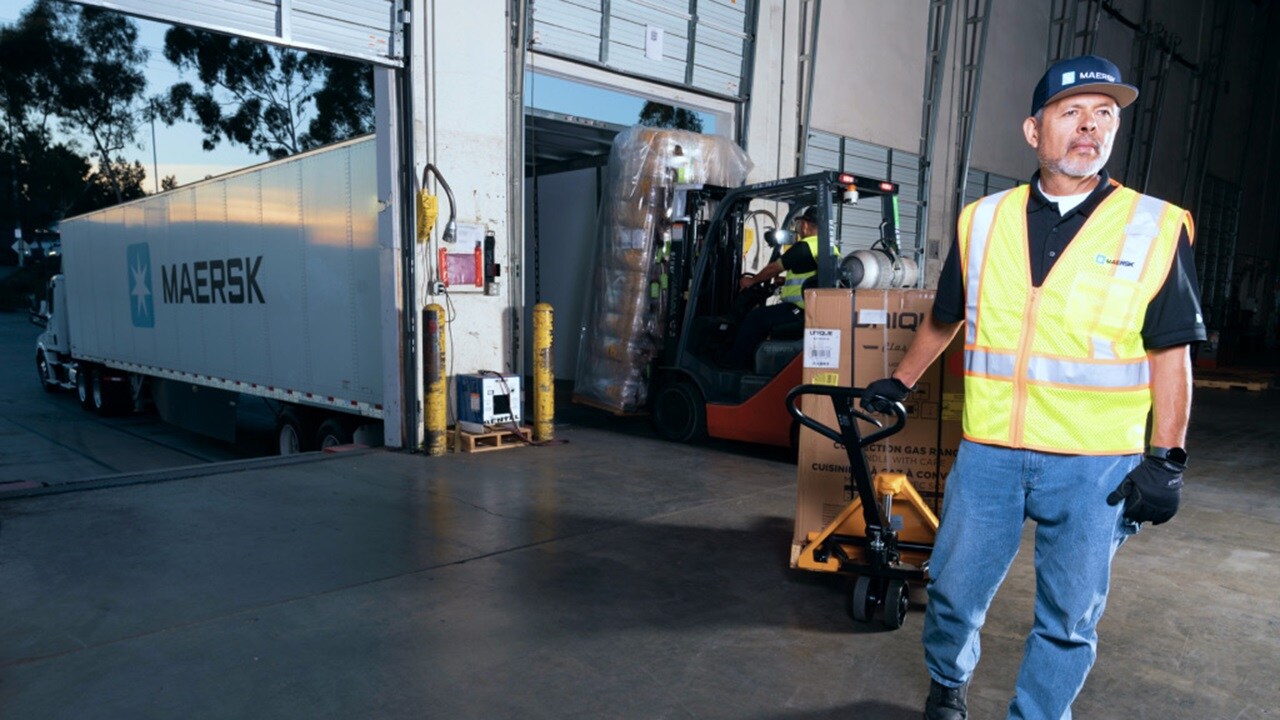 Warehouse workers driving a forklift, loading shipment cartons on a wooden pallet to Maersk container truck.